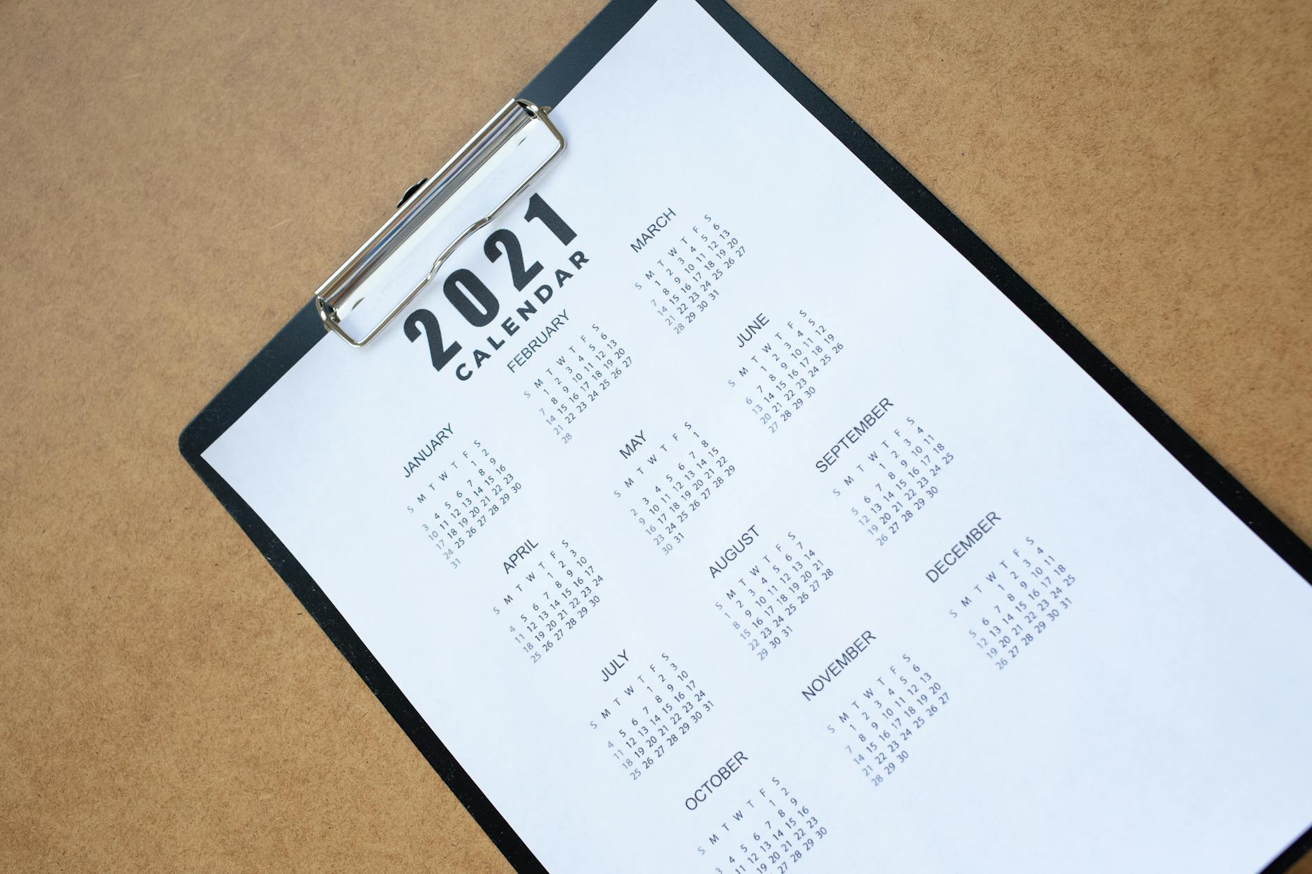 High angle shot of a 2021 calendar page clipped to a clipboard on a brown desk surface.
