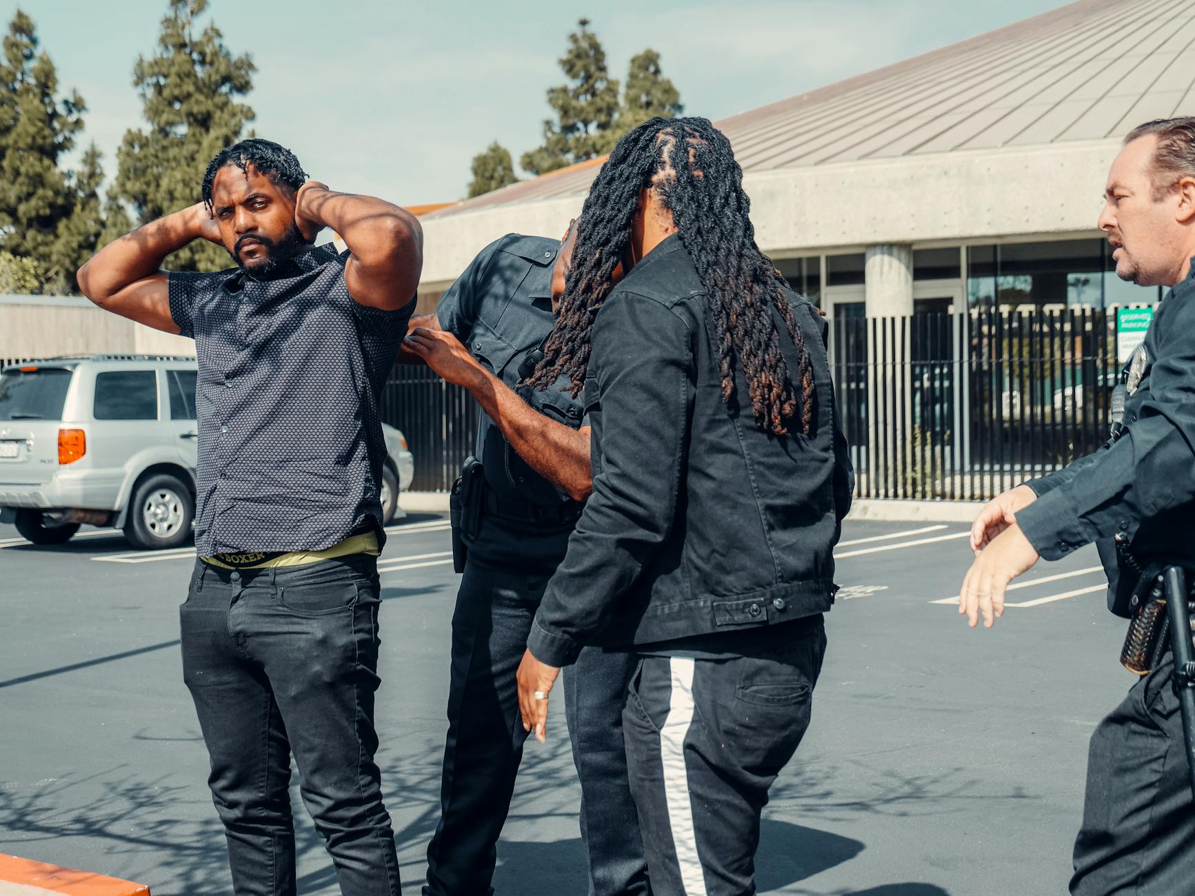 Two law enforcement officers detain a man during a daytime arrest outside a building.