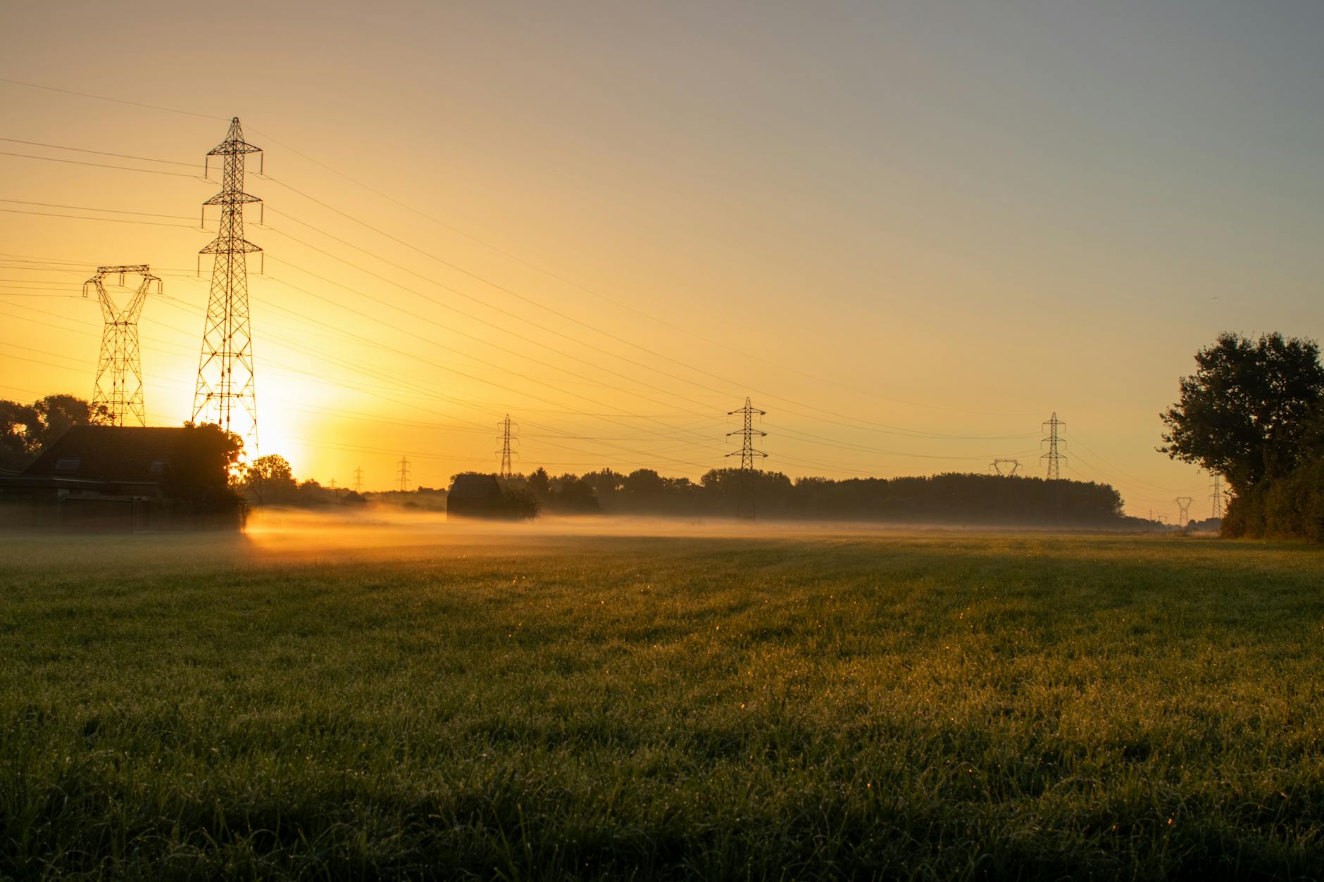 Sunrise over a rural field with fog and electricity pylons, creating a serene landscape.