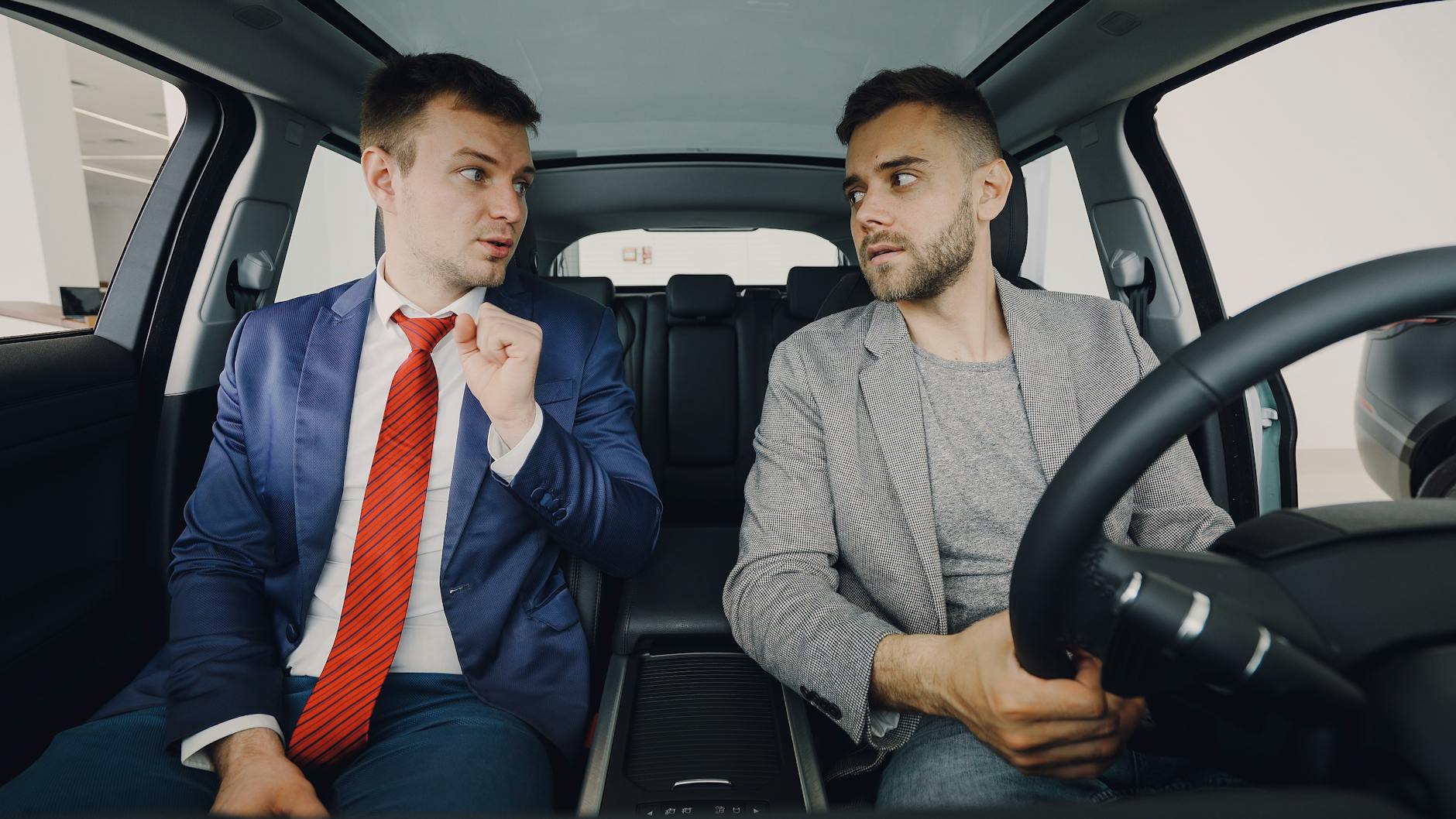Two businessmen in a car engage in conversation, focusing on discussion details.