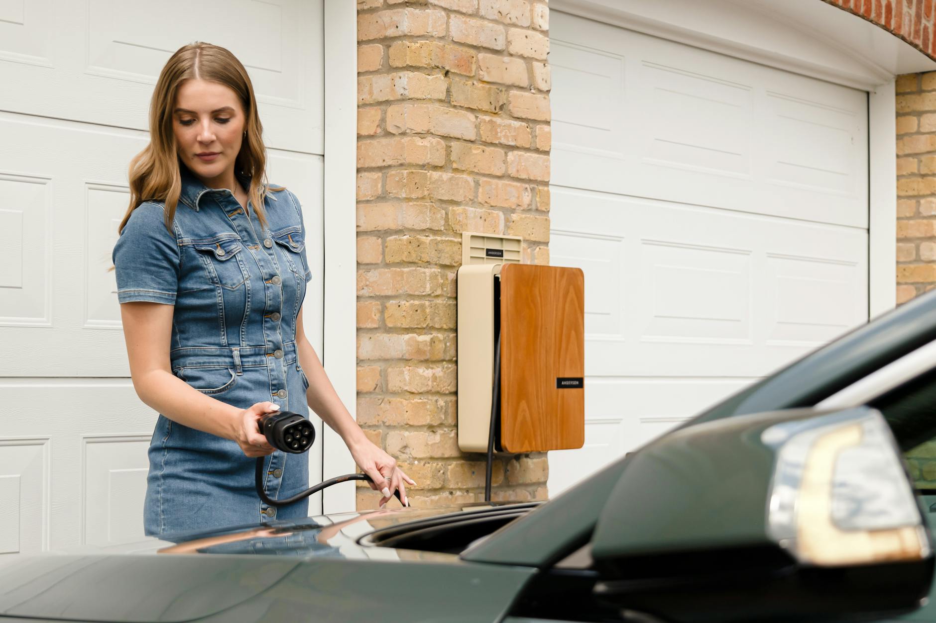 A woman plugs in an electric vehicle charger at a home charging station.
