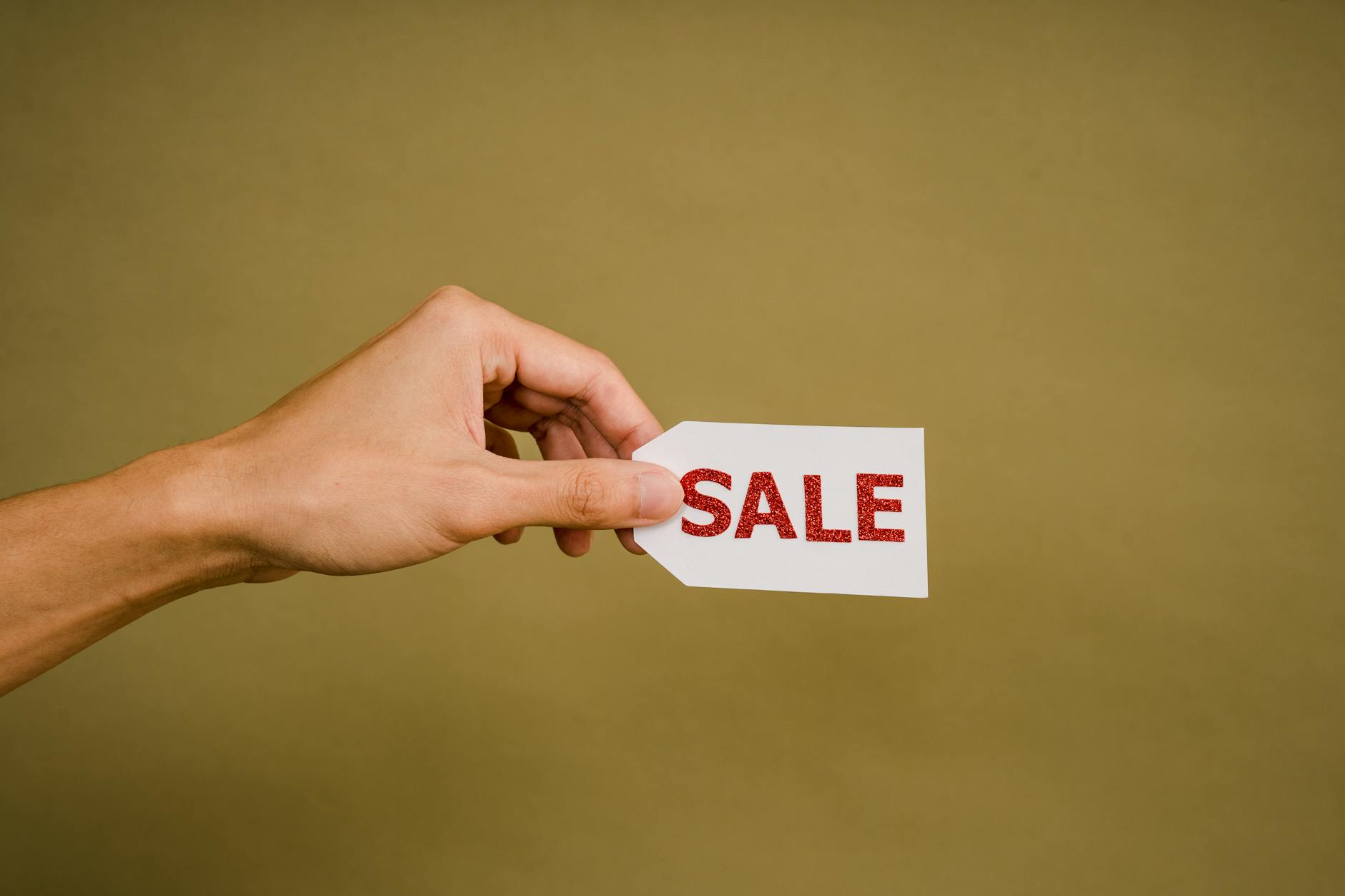 A hand holding a 'SALE' tag on a brown background, perfect for retail promotion.
