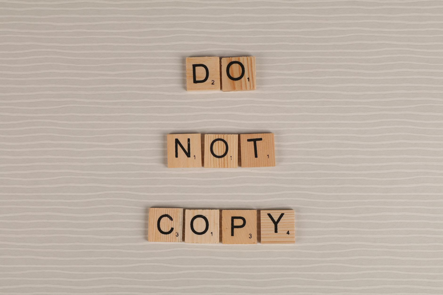 Close-up of wooden tiles spelling 'Do Not Copy' on a textured surface.