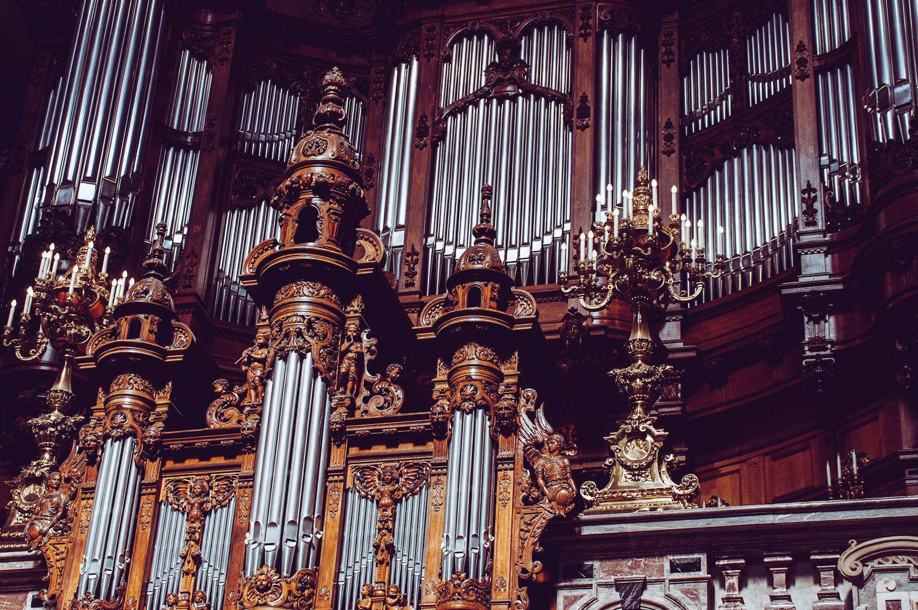 An intricate and ornate pipe organ inside a historic cathedral with decorative chandeliers.