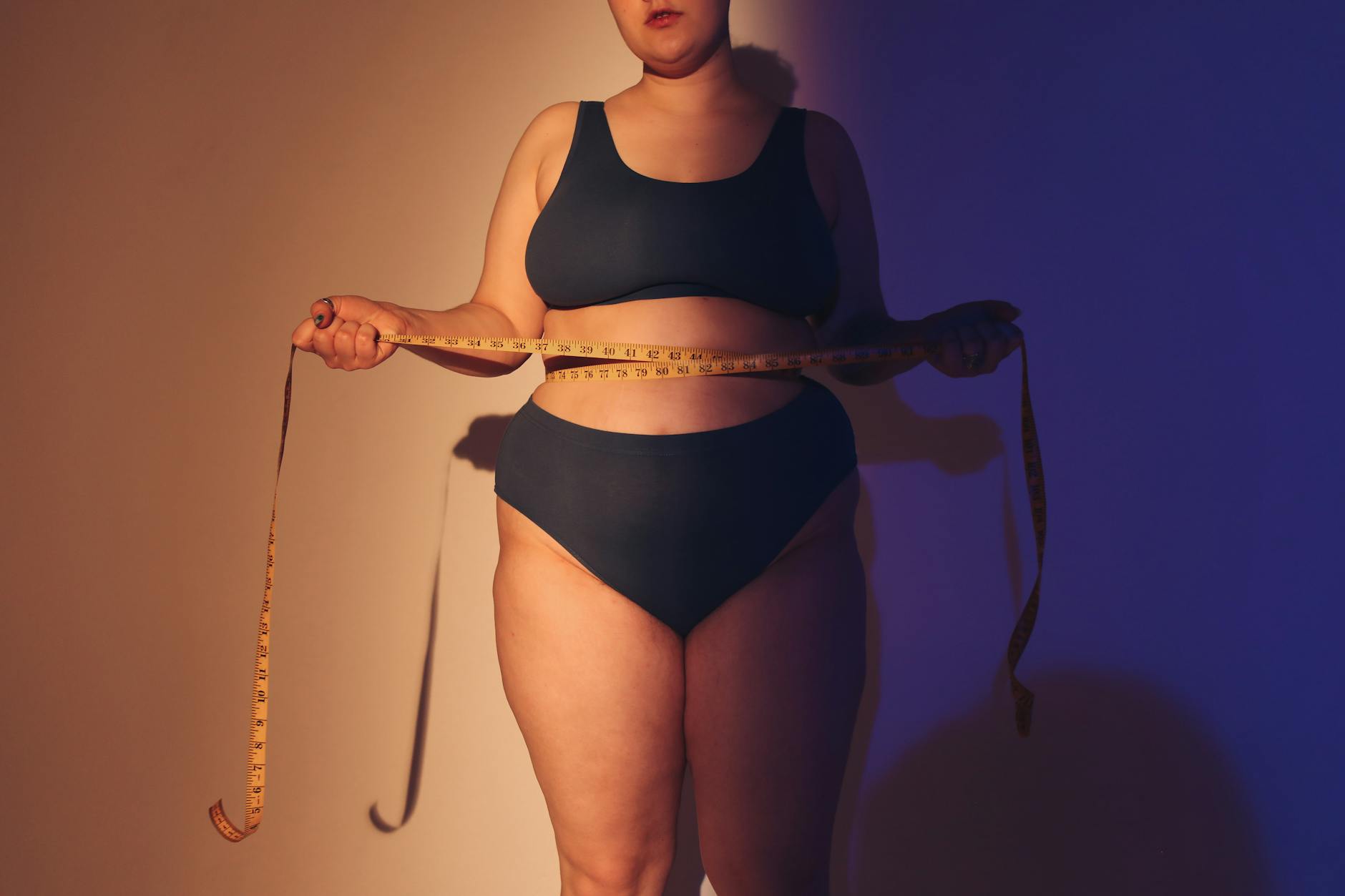 Confident plus size woman in studio holding a tape measure, emphasizing body positivity.