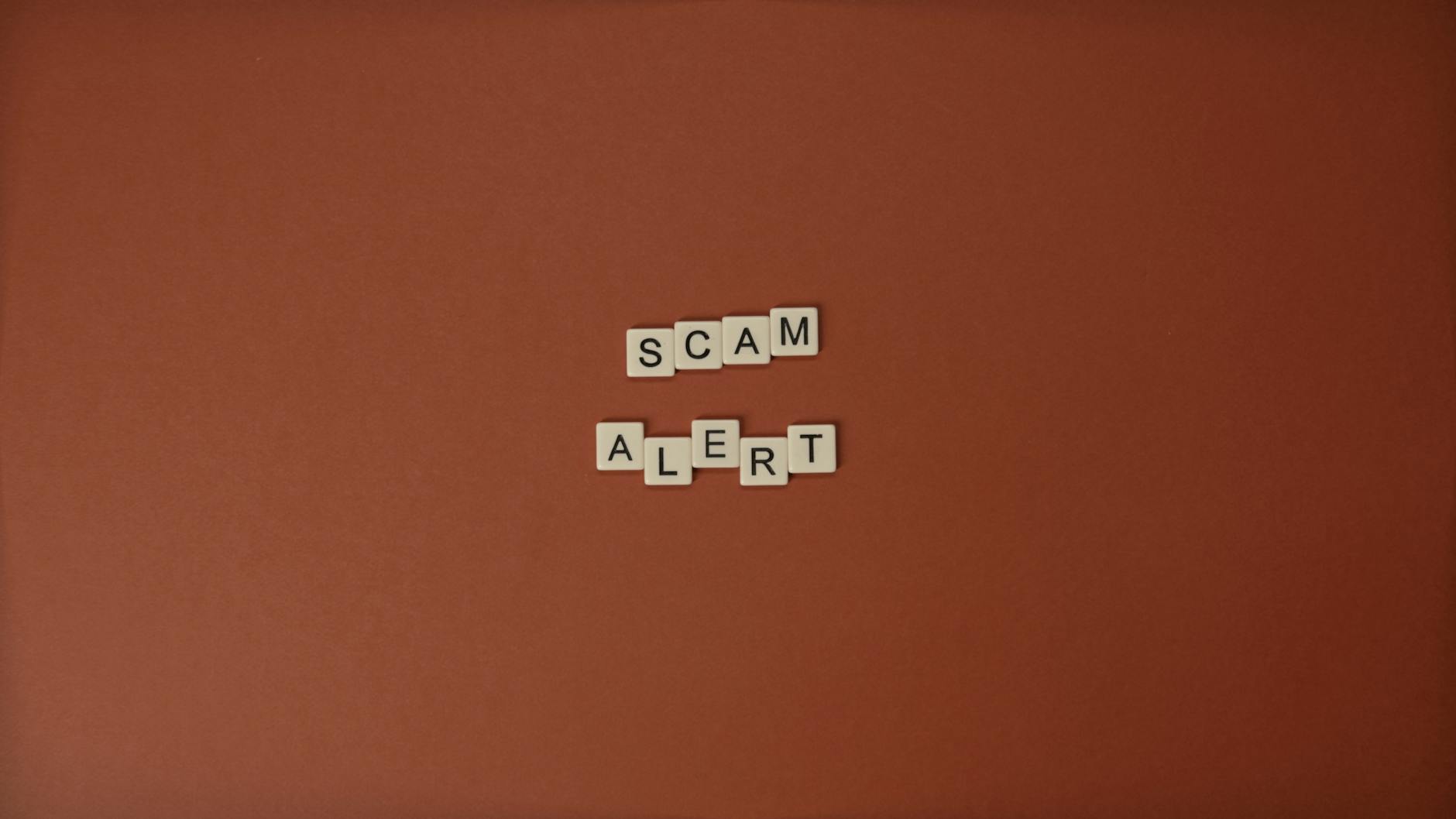 Scrabble tiles spelling Scam Alert on a brown surface indicating caution.
