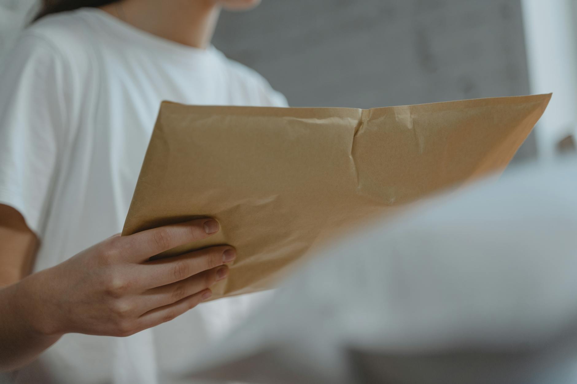 Close-up of a person holding a brown paper envelope, highlighting courier services or postal delivery indoors.