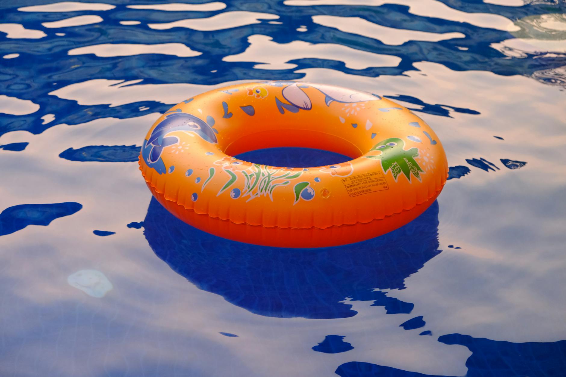 Orange inflatable ring floats on water in a sunlit pool, perfect for summer relaxation.